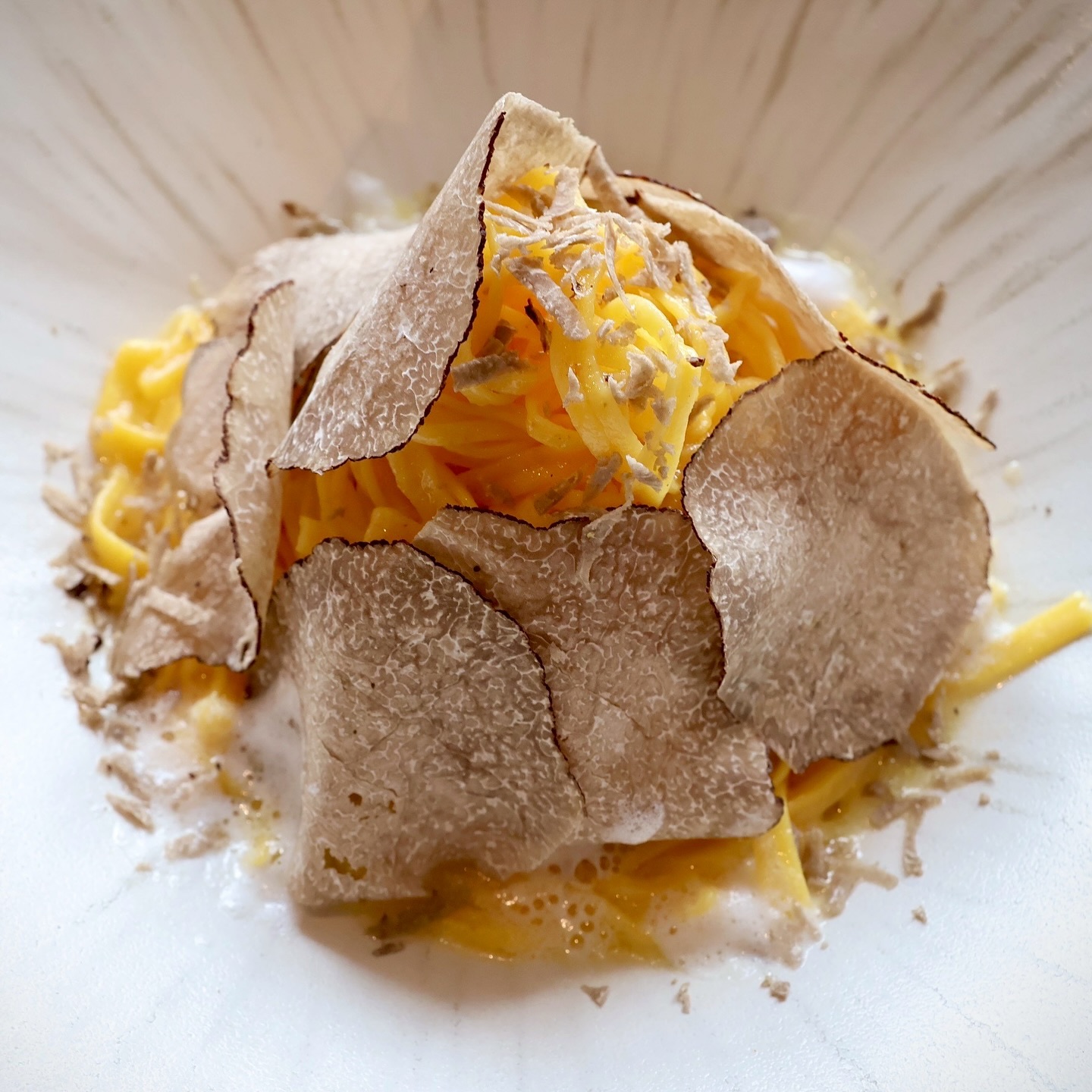 Hand-crafted golden tagliolini pasta tossed in a creamy sauce, generously topped with thin, aromatic shavings of fresh black truffle.